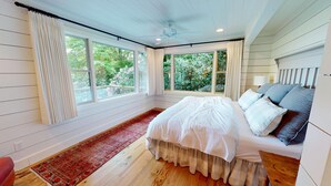 Quarto com uma cama grande, tapete vermelho e várias janelas com vista para o verde.