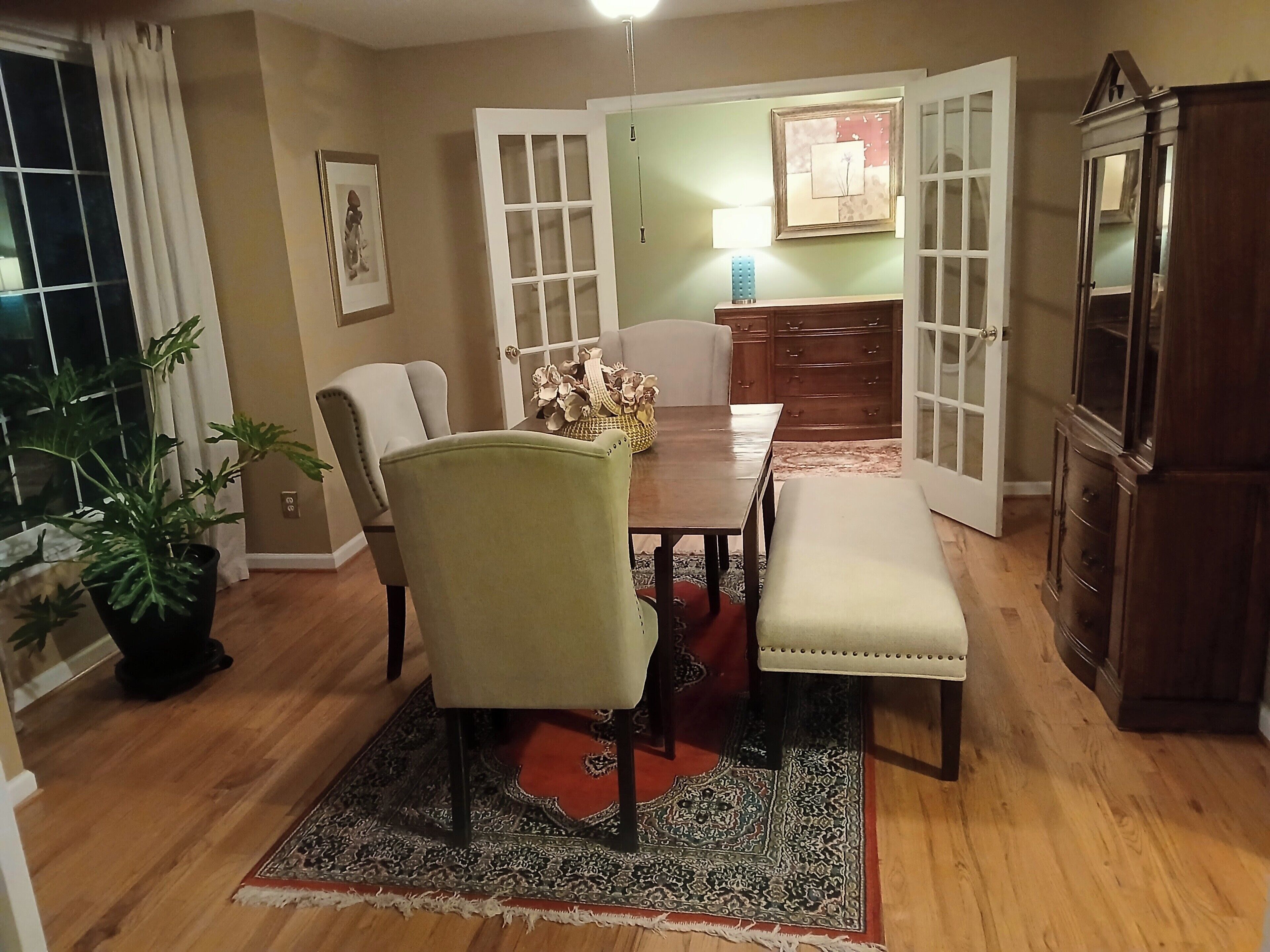 A dining area with a table, chairs, a bench, a cabinet, and a potted plant.