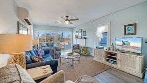 A living room with a sofa, coffee table, TV, and a view of the outdoors. - Family Tides by Seaside Vacations & Sales (Chincoteague Island)