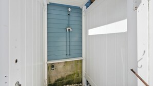 A small, enclosed shower area with a blue door and white walls. - Family Tides by Seaside Vacations & Sales (Chincoteague Island)