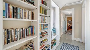 A hallway with white shelves filled with books, a blue striped rug, and a door leading to another room. - Family Tides by Seaside Vacations & Sales (Chincoteague Island)