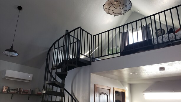 Un escalier en colimaçon avec une rampe noire, un luminaire au plafond et une porte dotée d’un miroir.