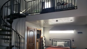 Une chambre à coucher comprenant un lit, un bureau, une chaise, une fenêtre, une porte et un escalier en colimaçon.