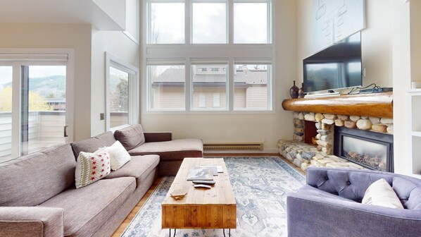 A living room with a stone fireplace, a sofa, a coffee table, and a television. - Knob Hill Ridge Townhome 1 - Modern Decor Right in Downtown and Pet Friendly (Ketchum)