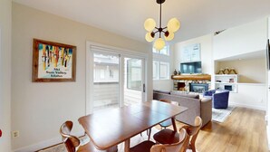 A dining area with a wooden table and chairs, a kitchen with a stone fireplace, and a living area with a sofa and TV. - Knob Hill Ridge Townhome 1 - Modern Decor Right in Downtown and Pet Friendly (Ketchum)