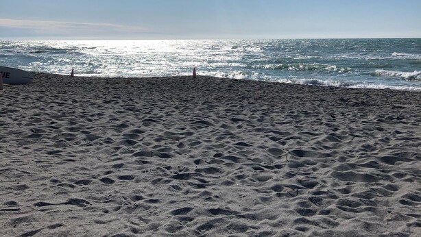 En sandstrand med fodaftryk, der fører ud i vandet, et redningstårn og et surfbræt.