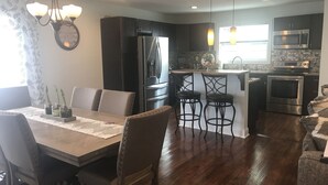 A modern kitchen with dark cabinetry, stainless steel appliances, a central island with bar stools, and pendant lighting.
