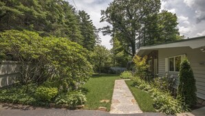 A residential property with a stone pathway leading to a house, surrounded by lush greenery and a wooden fence.
