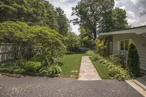 A residential property with a stone pathway leading to a house, surrounded by lush greenery and a wooden fence.