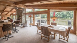 A spacious room with a large dining table, chairs, and a view of a lake through large windows.