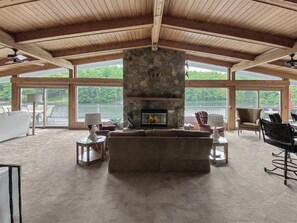 A spacious living room with a stone fireplace, large windows, and a view of a lake. - A Private Dock. A Lake That Goes Quiet After Sunset | Sequoyah Lakeside Lodge (Highlands)