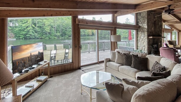 A spacious living room with a large TV, comfortable seating, and a view of a lake.