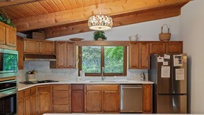 A kitchen with wooden cabinets, stainless steel appliances, a window with a view of greenery, and a hanging light fixture.