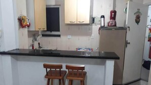 A kitchen with two wooden bar stools, a refrigerator, and a microwave. - Kit to enjoy the beach, holidays and vacations  (Praia Grande)