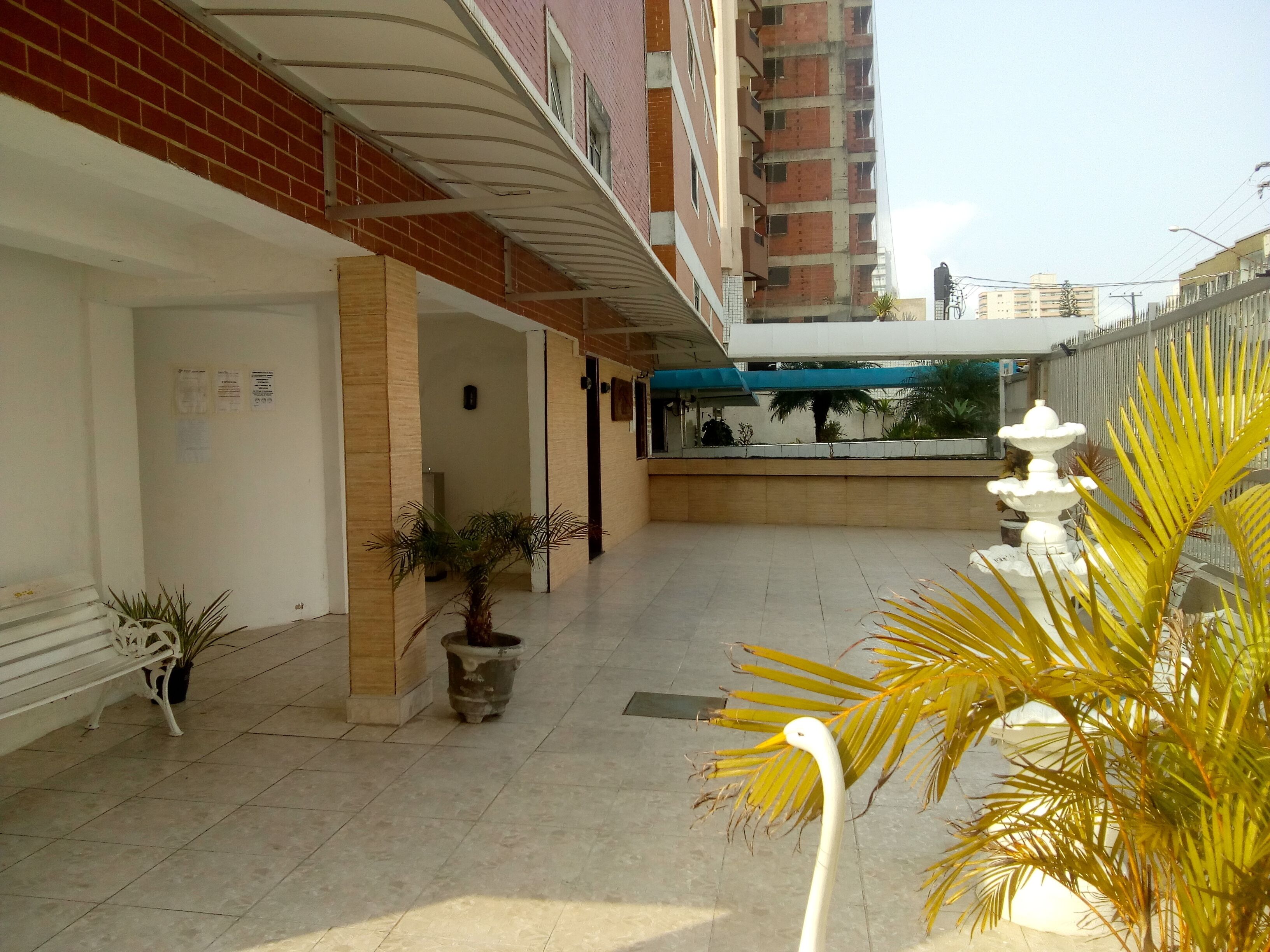 Un couloir d’hôtel avec un sol carrelé, des plantes en pot, un banc et une fontaine.