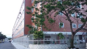 A multi-story building with a red brick facade, a gated entrance, and a tree in the foreground. - Kit to enjoy the beach, holidays and vacations  (Praia Grande)