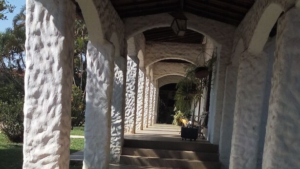 Un paseo techado con columnas blancas y suelo de baldosas que conduce a la entrada de un edificio.