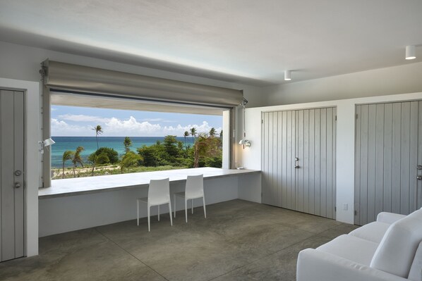 Una habitación moderna con un gran ventanal con vistas a la playa, un sofá blanco y una pequeña mesa con sillas.