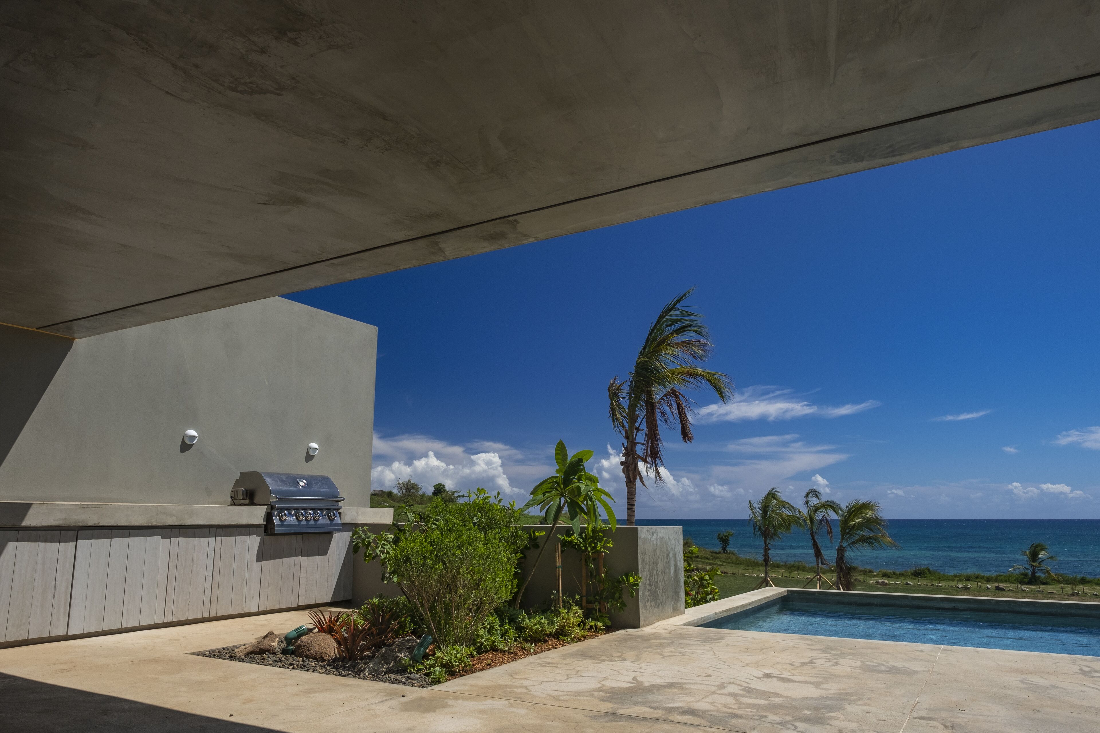 Un espace extérieur moderne doté d’une piscine, d’un barbecue et offrant une vue sur l’océan.