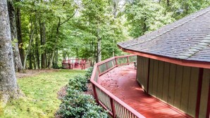 Une terrasse en bois dotée d’une balustrade incurvée, entourée d’une végétation luxuriante et d’arbres.