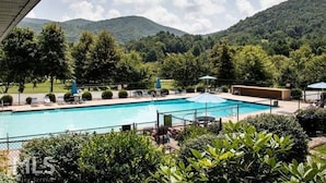 Une piscine entourée de verdure et de collines, avec des chaises longues et des parasols.