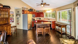 Une cuisine avec des meubles de rangement en bois, un îlot central, un ventilateur de plafond et une fenêtre avec des stores.