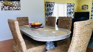 A dining area with a round table, wicker chairs, and a bowl of fruit. - Relaxing beach vacation - beautiful, quiet and clean (Cooks Beach)