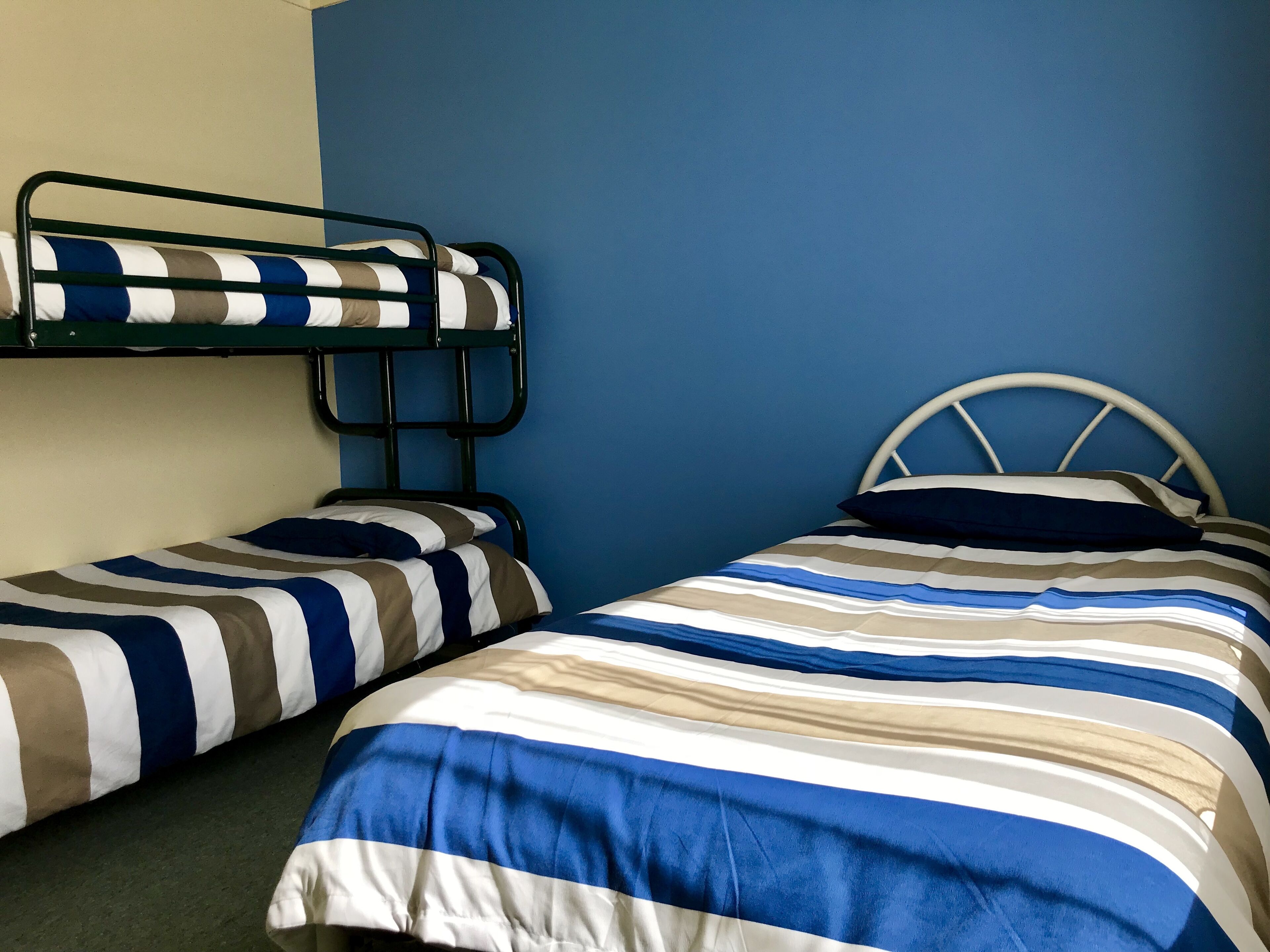 Una habitación con dos literas, cada una con ropa de cama a rayas, frente a una pared azul.