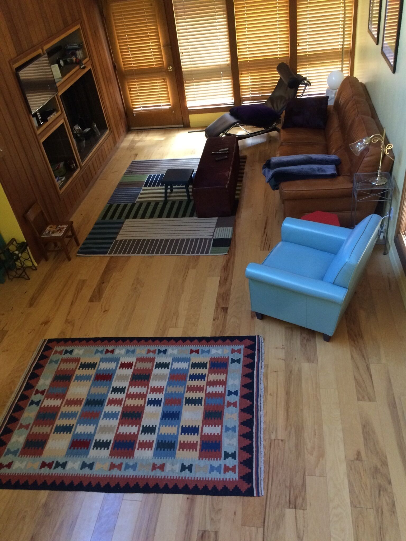 Uma sala de estar com piso de madeira, um sofá azul, um estofado de couro marrom e um tapete estampado.