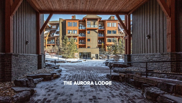 A view of The Aurora Lodge with a stone pathway leading to the entrance, wooden beams, and a multi-story building with balconies.