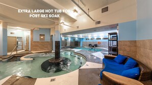 A large indoor hot tub with a stone pillar, surrounded by a blue and beige color scheme, and a wicker sofa with blue cushions.