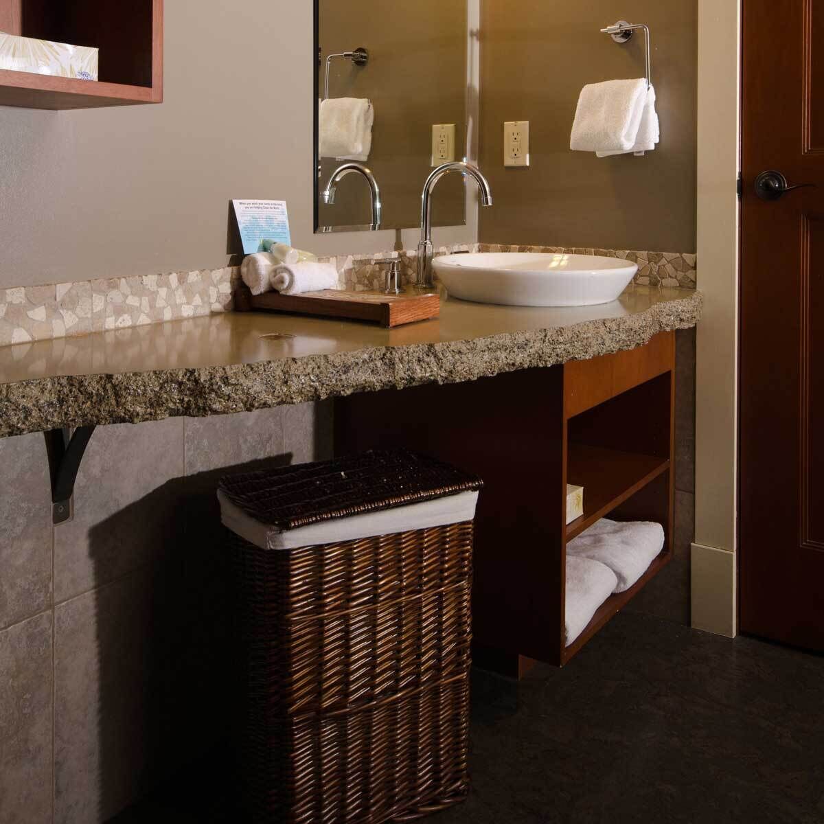 A bathroom with a granite countertop, a white sink, a mirror, and a wicker trash bin.