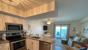 A modern kitchen with stainless steel appliances, a dining area with a view of the ocean, and a cozy living room with a patterned sofa. - Beautiful Renovated Gulf Front Condo! (Gulf Shores)