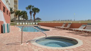 A pool area with two hot tubs, lounge chairs, and a building in the background. - Beautiful Renovated Gulf Front Condo! (Gulf Shores)