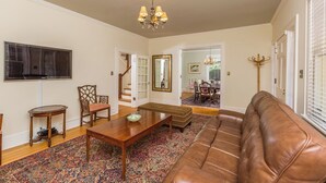 Un salon avec un canapé en cuir marron, une table basse en bois, un téléviseur fixé au mur et un escalier menant à une autre pièce.