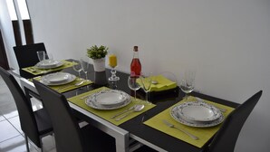 Uma mesa de jantar posta com pratos, talheres e copos, com uma pequena planta e uma garrafa de vinho tinto sobre a mesa.
