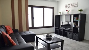 Uma sala de estar moderna com um sofá preto, uma mesa de centro, uma TV em um suporte preto e um letreiro com a palavra 'HOME' na parede.