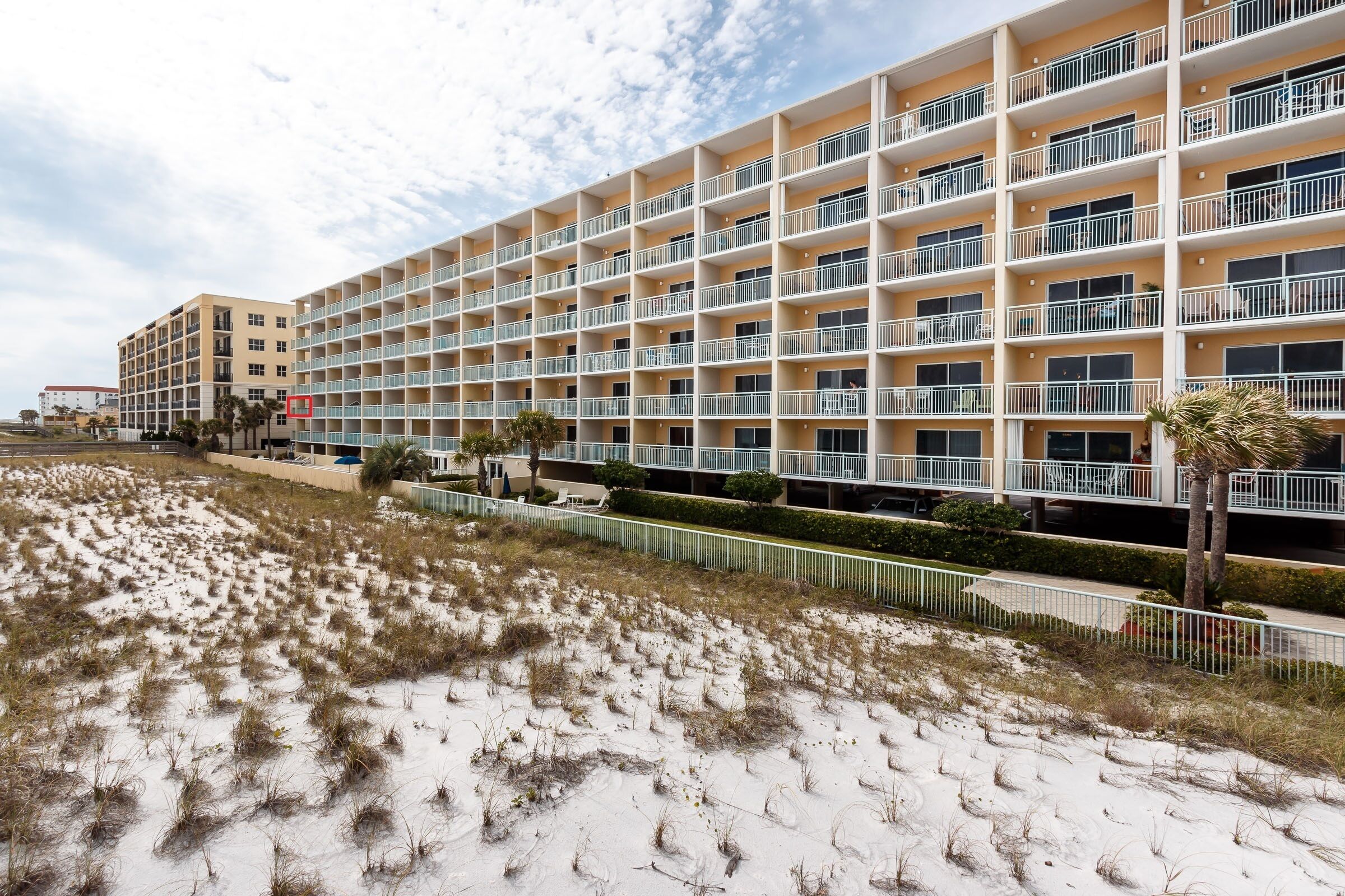 Un hotel a più piani con facciata uniforme, balconi e una spiaggia sabbiosa in primo piano.