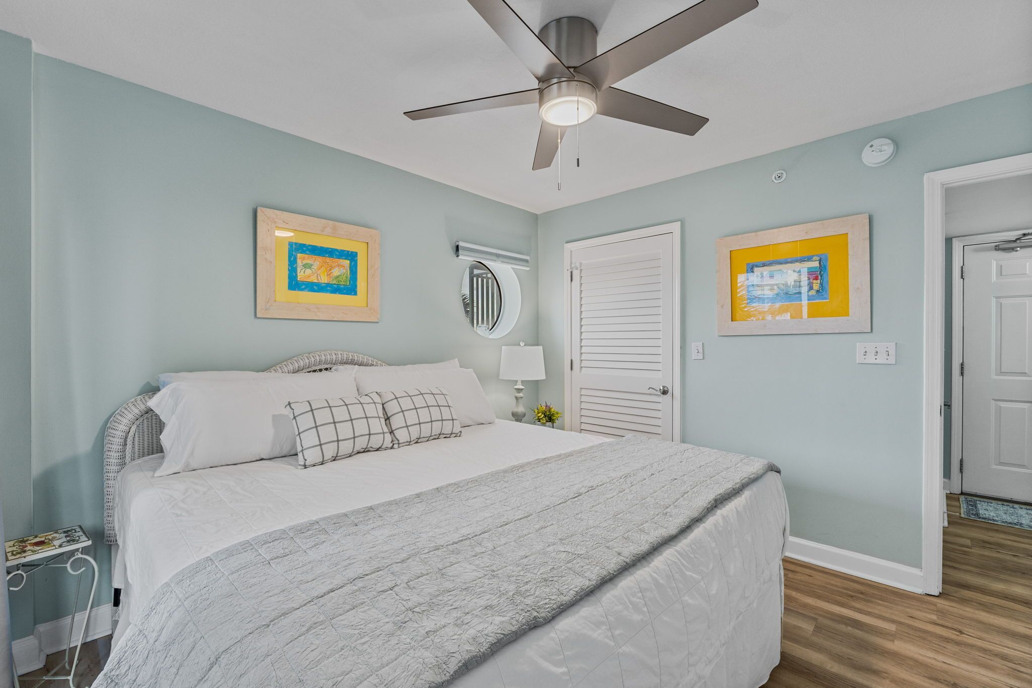 Une chambre à coucher avec un lit, un ventilateur de plafond, des œuvres d’art et une porte.