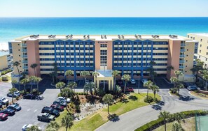 A hotel with a central entrance, multiple floors, and a parking lot with several cars. - PI 218: Beach Vibes Only -Rare End Unit~Wrap-Around Balcony~2 King Beds+Bunks (Fort Walton Beach)