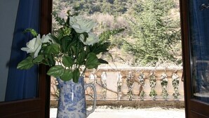 A room with a view of a mountainous landscape through a large window with blue curtains. A vase with white flowers is placed on a wooden table. - Spacious Three Bedroom Mountain Villa with Pool (Serdinya)