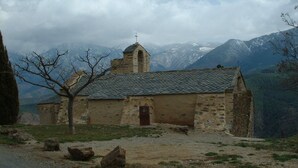 A rustic stone building with a sloped roof, a small bell tower, and a door. It is surrounded by a natural landscape with mountains in the background. - Spacious Three Bedroom Mountain Villa with Pool (Serdinya)