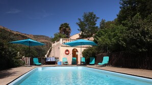 A swimming pool with blue umbrellas, lounge chairs, and a wooden deck. - Spacious Three Bedroom Mountain Villa with Pool (Serdinya)