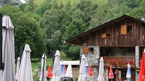 Un bâtiment rustique en bois, doté d’une façade en pierre, entouré d’une végétation luxuriante et avec une cascade en arrière-plan.