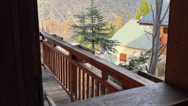 Un balcon en bois offrant une vue sur un paysage montagneux et une maison dotée d’un toit végétalisé.