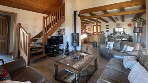 Un vaste salon doté d’un escalier en bois, d’une cheminée, d’un téléviseur et d’un coin cuisine à l’arrière-plan.