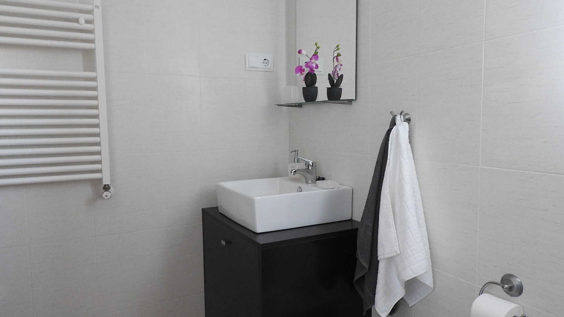 A bathroom with a white sink, dark cabinet, and a towel rack.