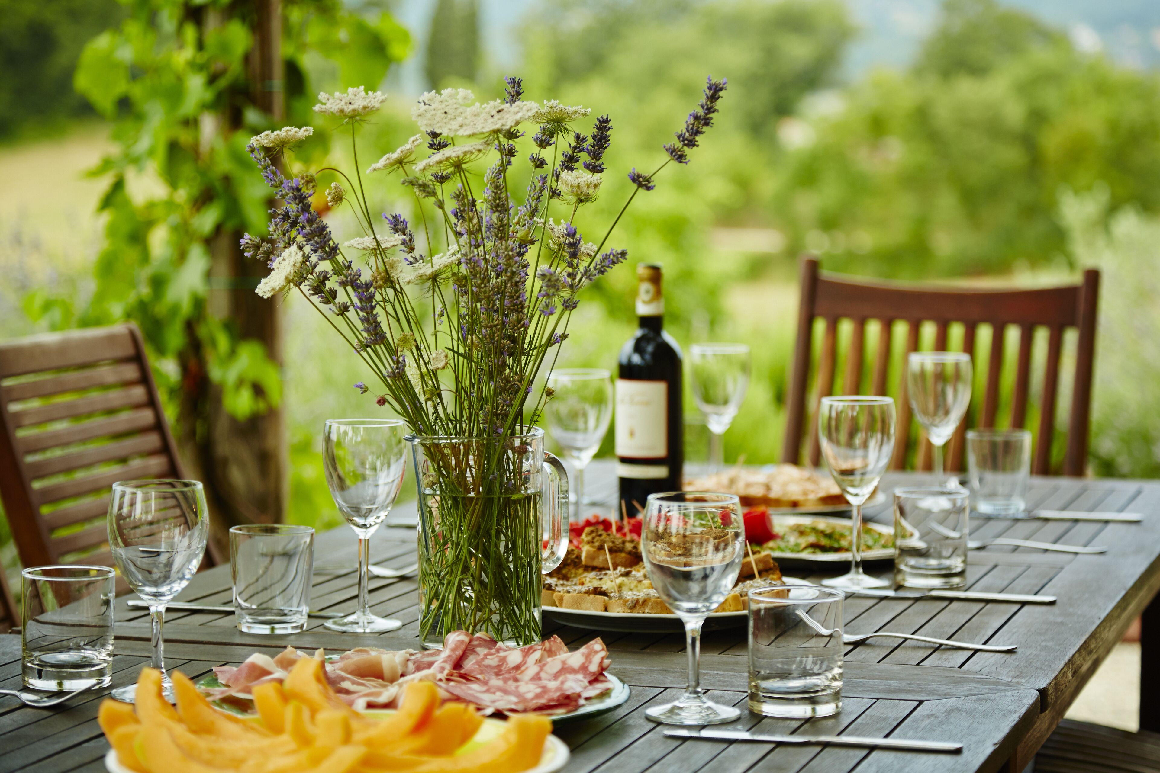 A wooden table set for a meal with plates of food, glasses, and a bottle of wine.