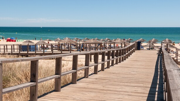 Um calçadão de madeira que leva a uma praia com guarda-sóis e cadeiras de praia.