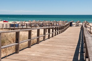 A wooden boardwalk leading to a beach with umbrellas and beach chairs. - Holiday 2 Bedroom Apartment with balcony (Alvor)
